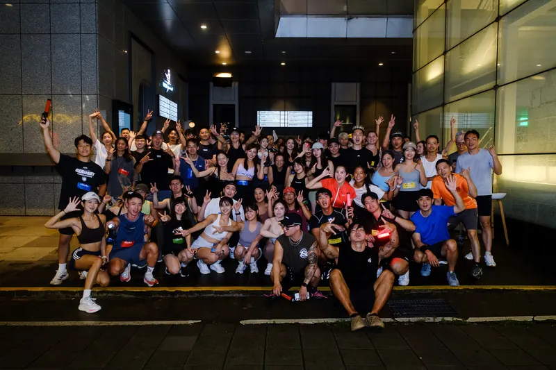 A large group of runners posing together with arms raised at night.