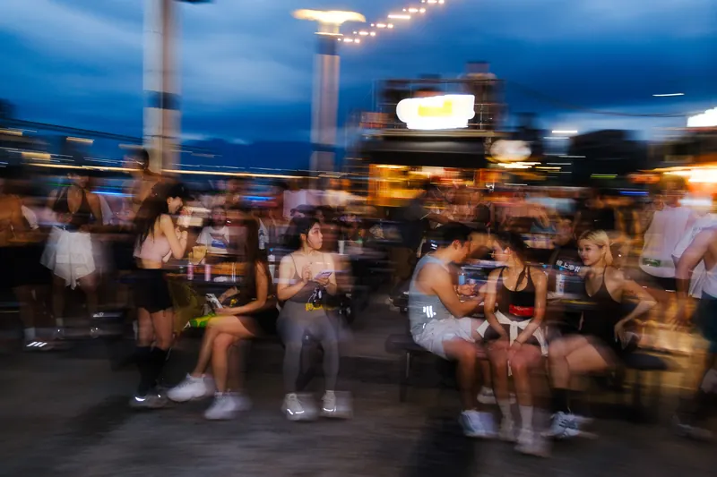A crowd at an outdoor party at dusk, blurred by motion under string lights.